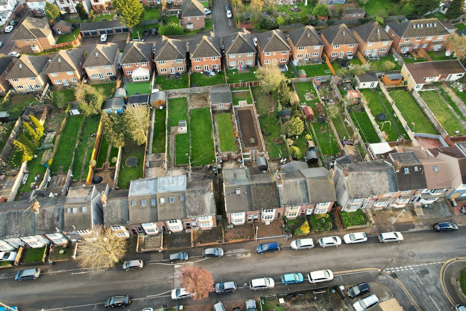 An aerial view of a row of terraced houses along Yeading Lane, showing neatly maintained back gardens with a variety of features. The gardens include lush green lawns, some bordered with wooden fences